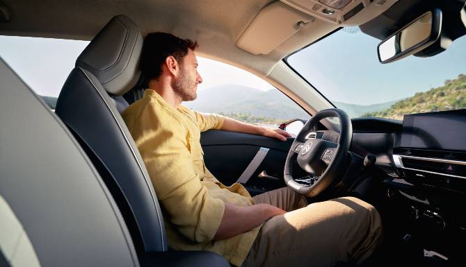 Man driving a car, wearing a yellow shirt, viewed from the passenger seat.