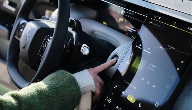Person pressing start button in a car with a touchscreen dashboard display.