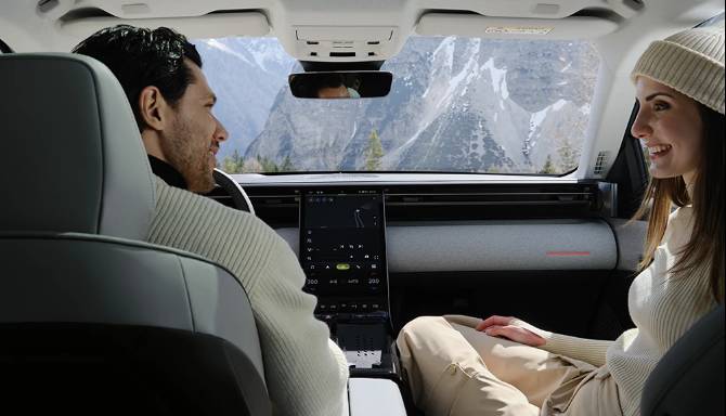 Two people sitting in a car, facing each other and smiling, with a mountain view in the background.