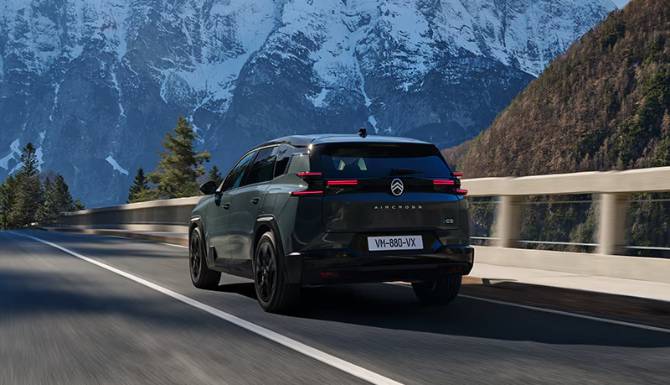 A Citroën SUV driving on a mountain road with snowy peaks in the background.