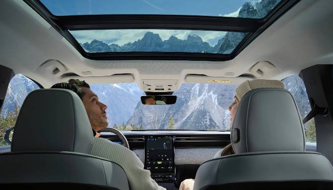 Two people in a car with a panoramic sunroof, viewing a mountain landscape.