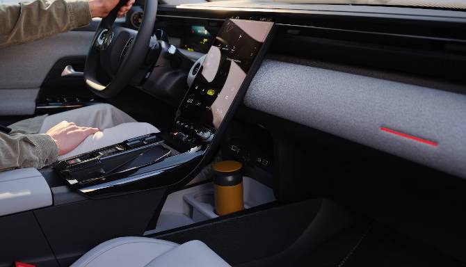 Car interior with a touchscreen display and a person driving.