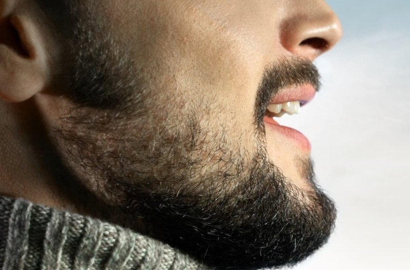 Close-up of a bearded man's profile wearing a grey ribbed turtleneck sweater.