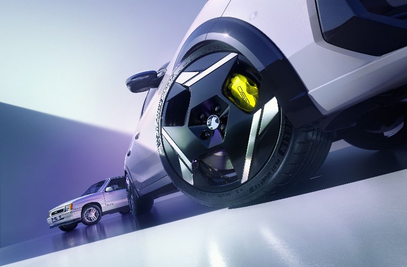 Close-up of a car's front wheel with a yellow brake caliper and another car in the background.