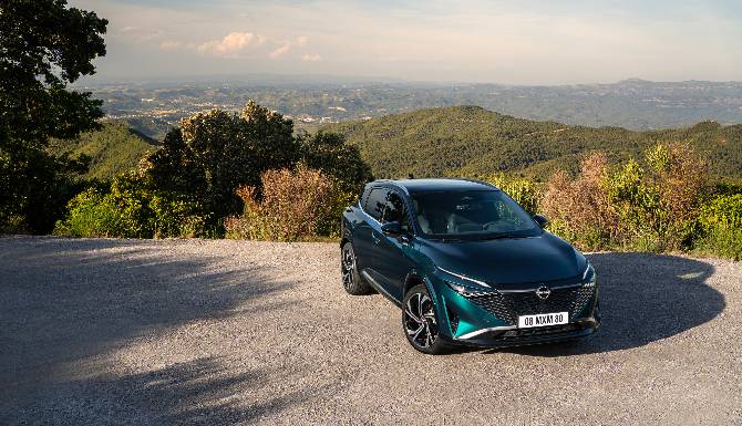 A blue car parked on a gravel road with a view of hills and trees.