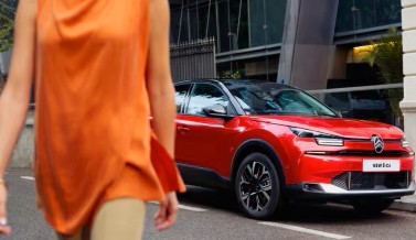 Person walking past a red car parked on a city street.