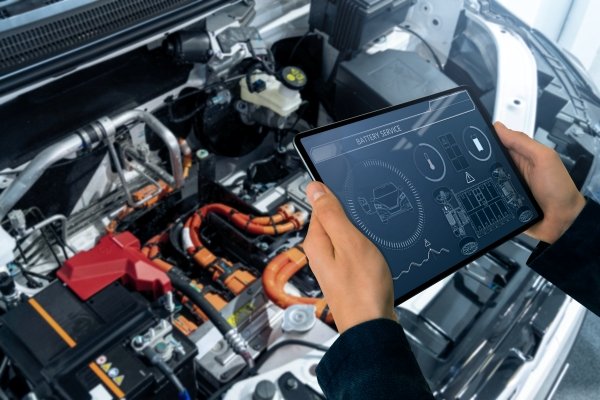 Person using tablet to monitor an electric car battery under the bonnet.