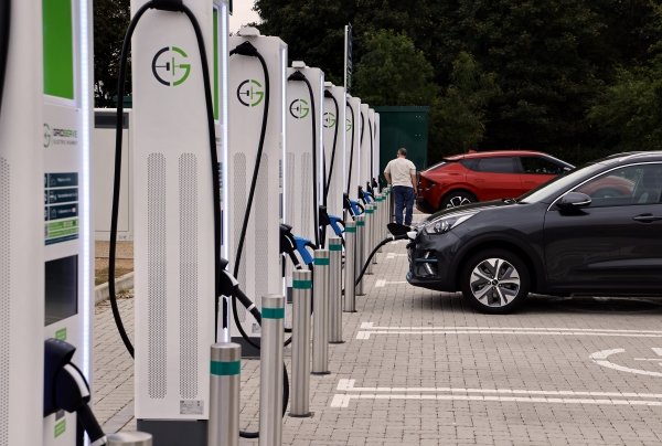 Electric vehicle charging stations in a row with cars parked nearby.