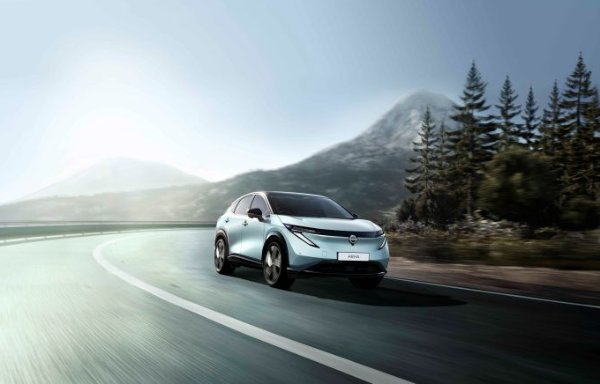 Electric car driving on a curving mountain road with trees and hills in the background.