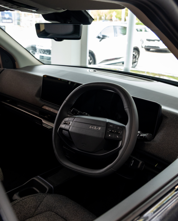 Kia car interior showing steering wheel, dashboard, and driver's seat from the side.