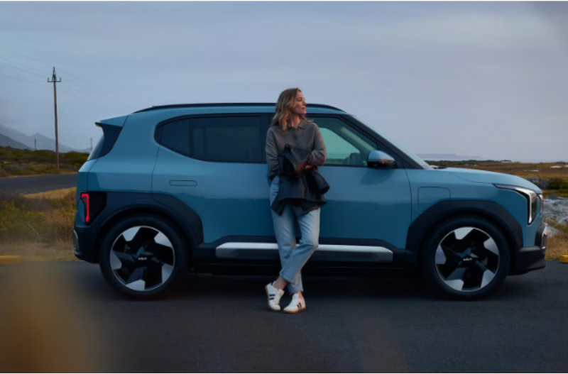 Woman leaning against a parked, modern compact SUV on a scenic road.