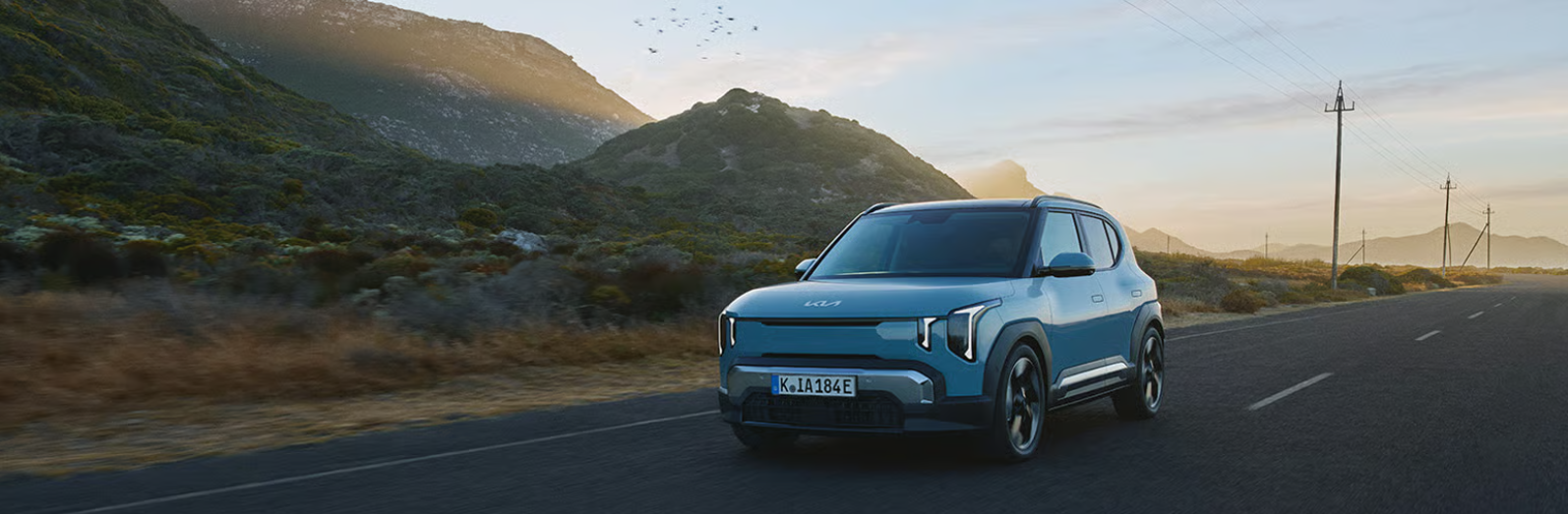 Blue SUV driving on a road with mountains in the background.