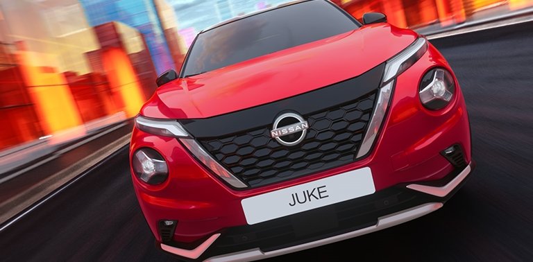 Front view of a red Nissan Juke driving on a road with colourful buildings.