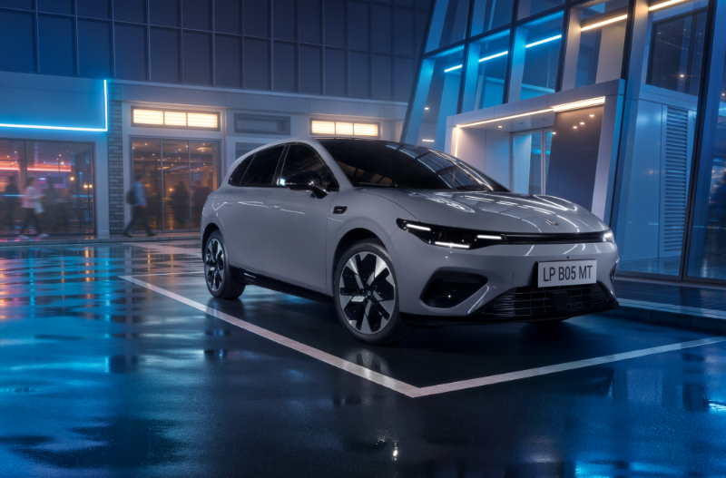Grey electric car parked in front of a modern glass building at night.