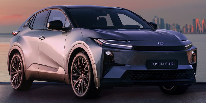 Grey Toyota C-HR parked near a waterfront with city skyline at sunset.