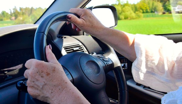 Hands of an older person holding a steering wheel while driving a car.