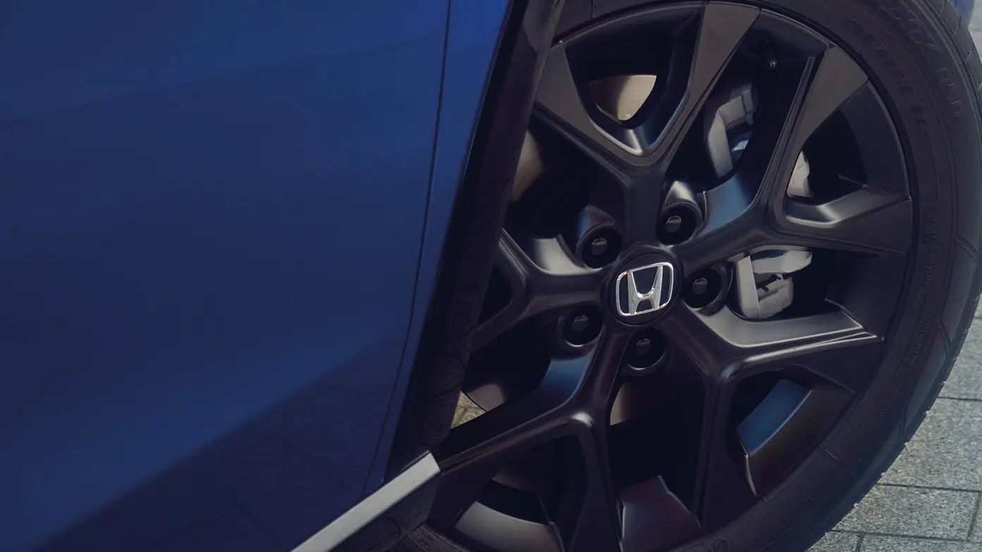 Close-up of a black alloy wheel with the Honda logo on a blue car.