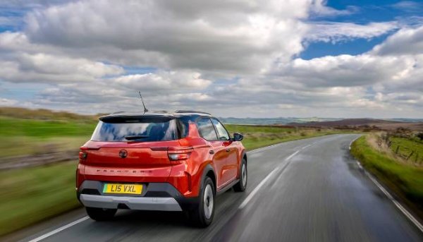Red car driving on a countryside road under a cloudy sky.