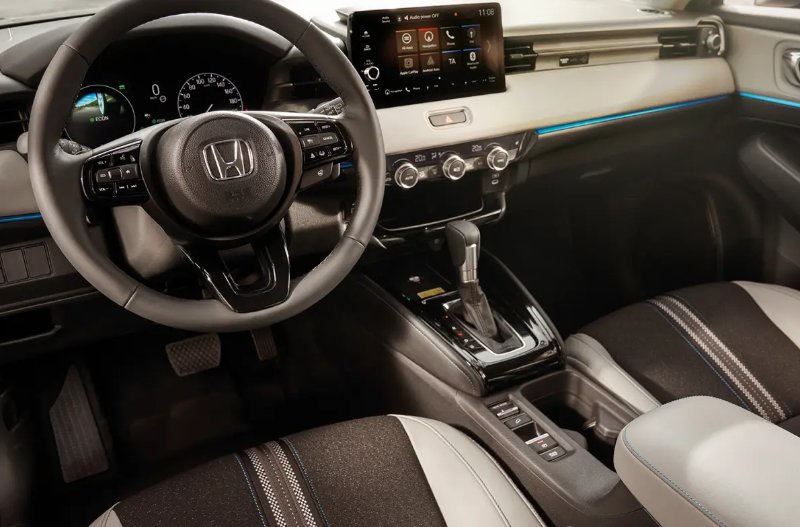 Car interior showing steering wheel, infotainment screen, gear shift, and dashboard controls.