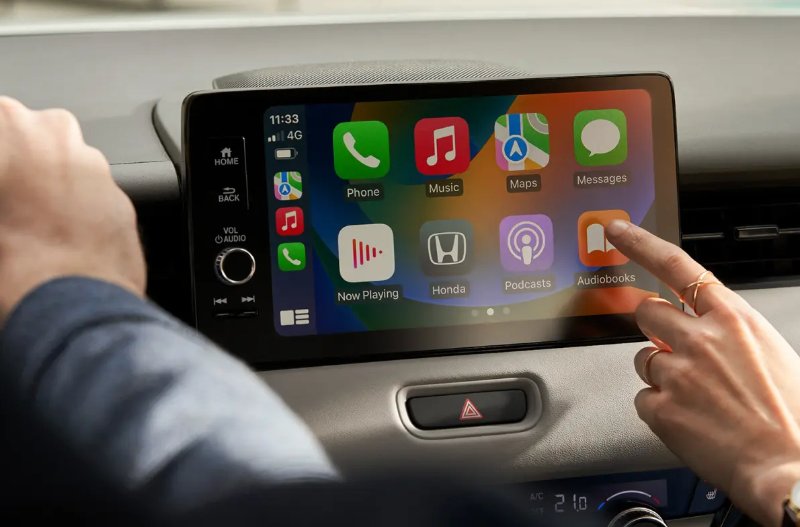 Person interacting with a car touchscreen display showing various app icons.