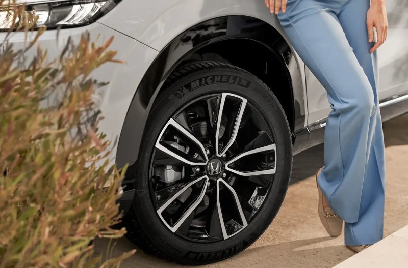 Person in blue trousers standing by a car tyre showing its alloy wheel design.