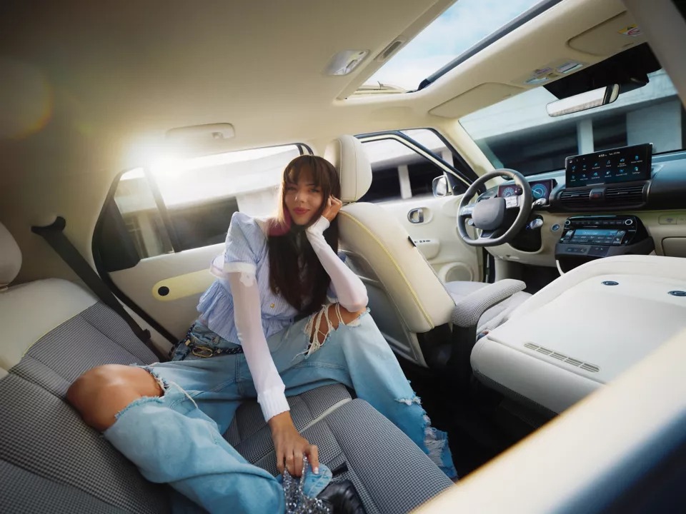 Woman sitting in a car's back seat, sunlight streaming through the window and sunroof.
