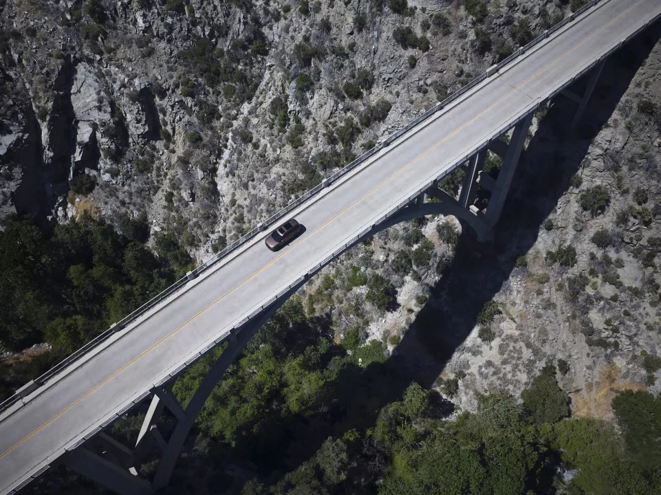 A car crossing an arched bridge over a rocky landscape.