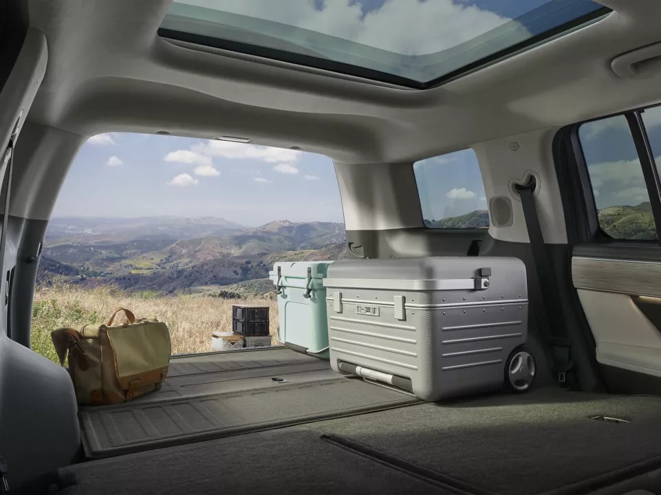 Open car boot with luggage, coolers, and scenic mountain view through the sunroof.