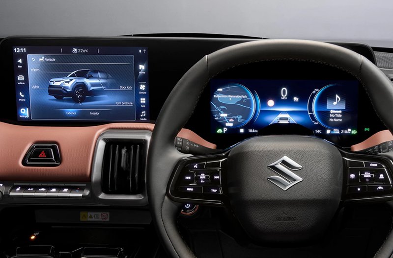 Car dashboard showing digital displays behind a steering wheel with a Suzuki logo.