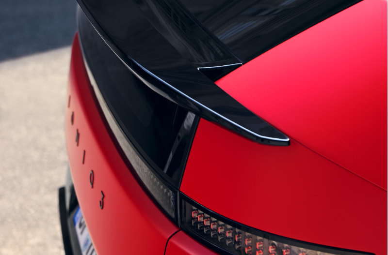 Close-up of the rear spoiler and taillight of a red car in daylight.