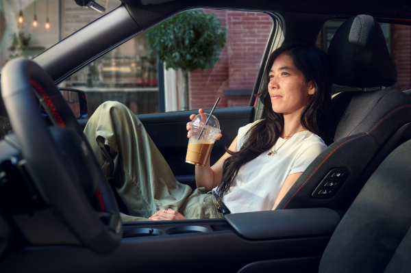 Person relaxing in a car passenger seat, holding an iced coffee.