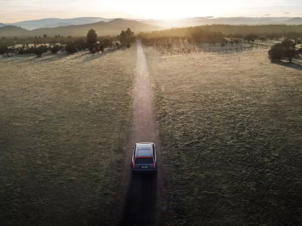 Car driving on a country road at sunrise with fields on either side.