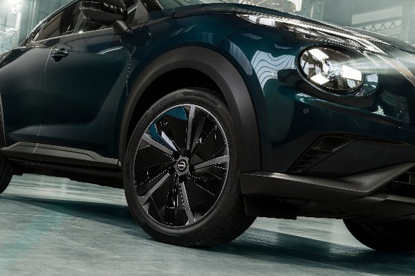 Close-up of black alloy wheel and headlight of a dark-coloured car.