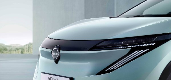 Close-up of the front of a Nissan Ariya car showing logo and headlight detail.
