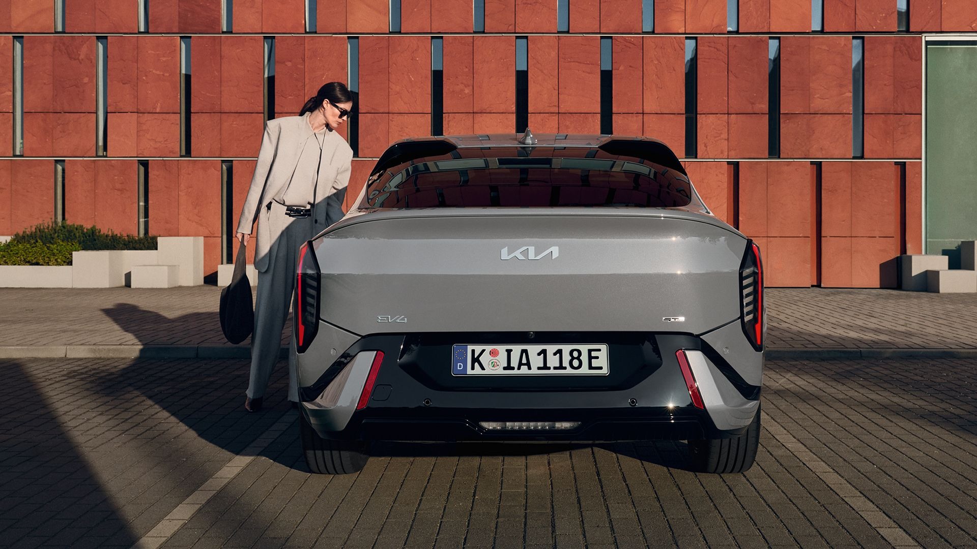 Person in sunglasses stands beside a grey Kia EV4 car.