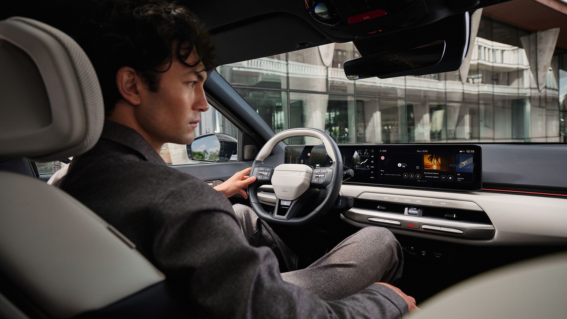 Man in a car, holding the steering wheel, with a digital dashboard display visible.