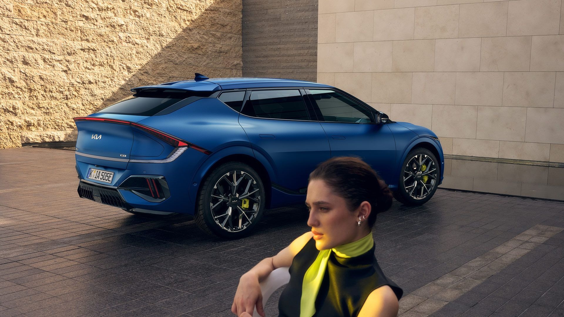 Blue electric car parked beside a building, with a person in the foreground.