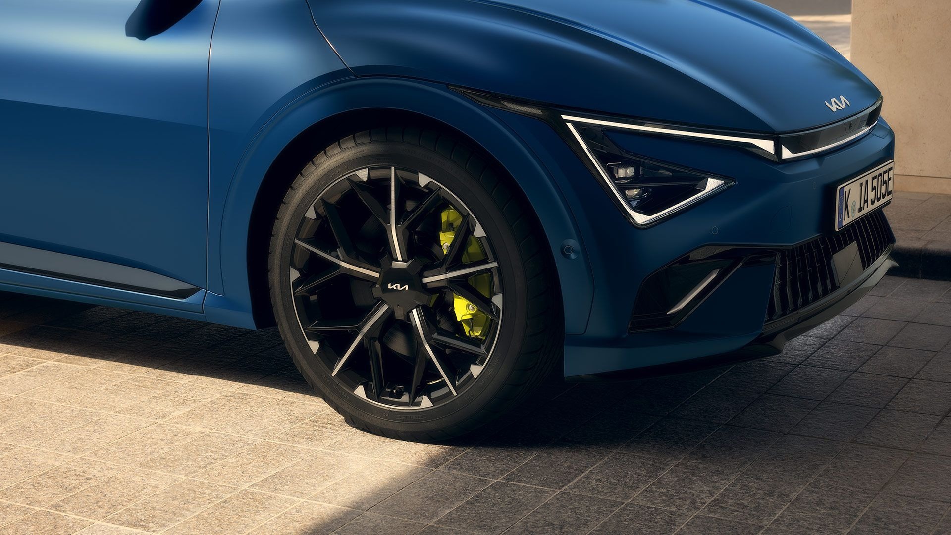 Close-up of a blue car with black alloy wheel and visible front lights.