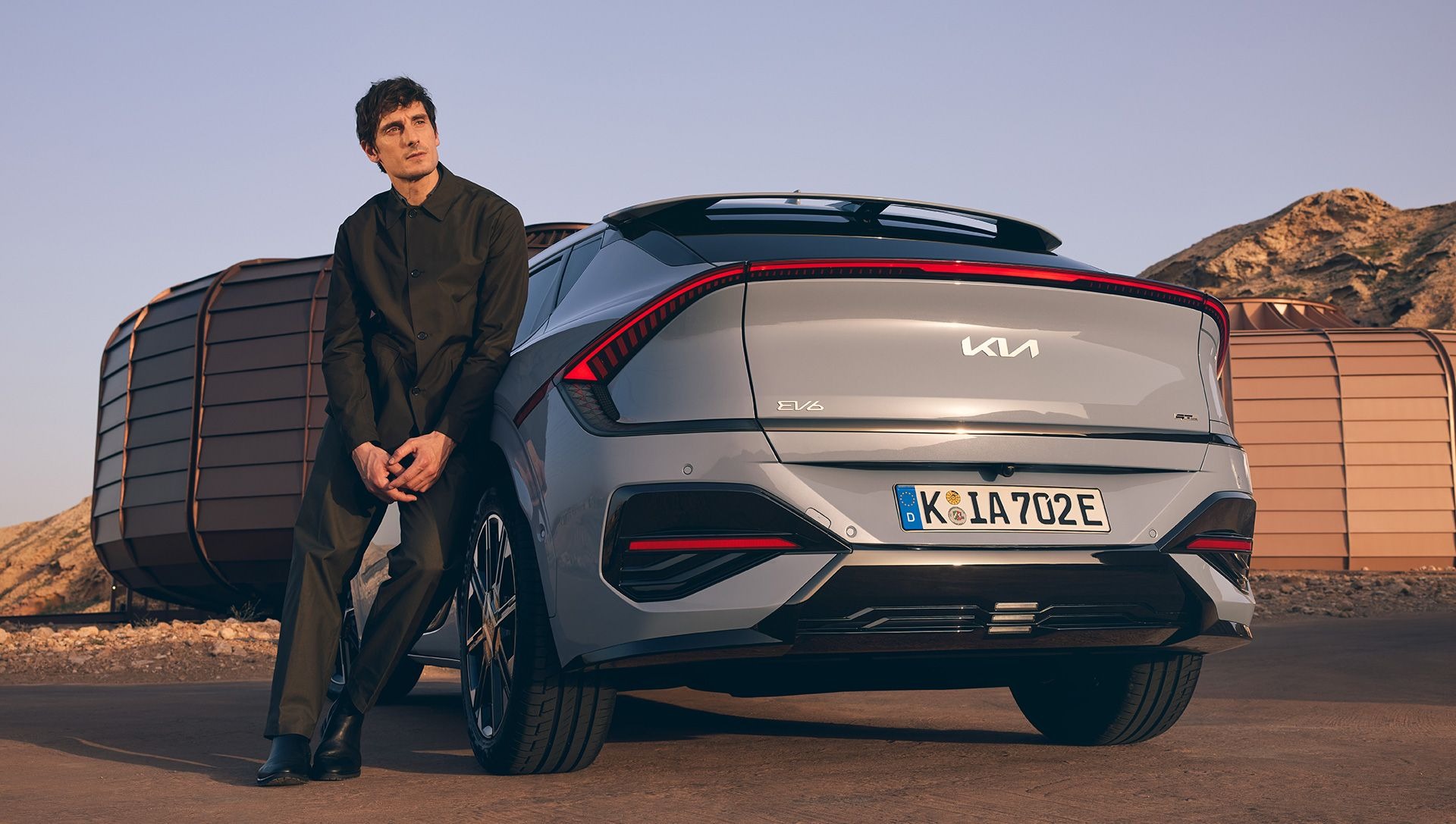 Man leaning on silver Kia EV6 GT-Line parked on a road.