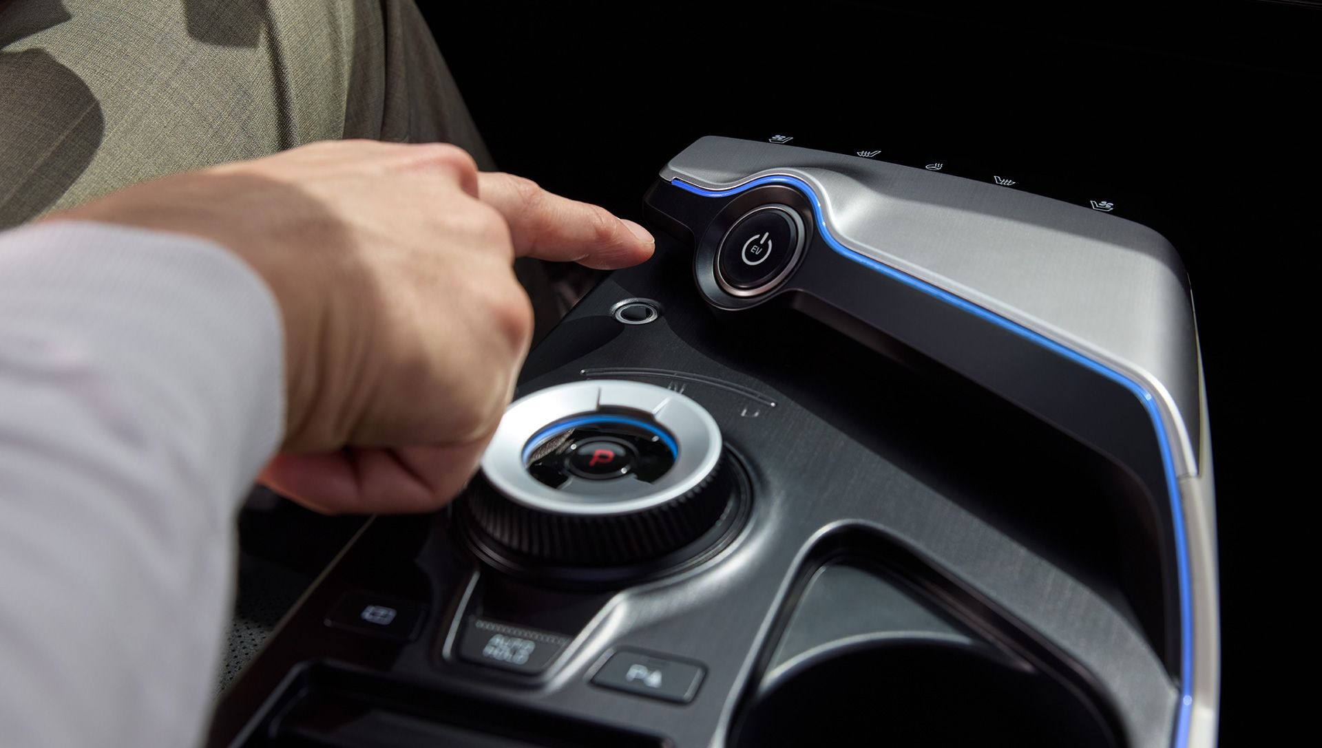 Hand reaching to press a start button on a car's centre console.