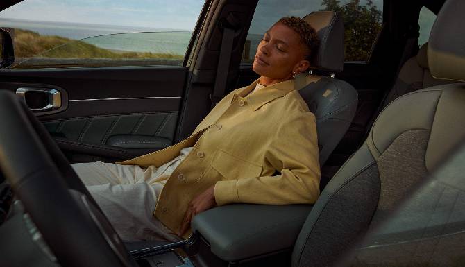 Person relaxing in a car seat, wearing a beige jacket and resting against the headrest.
