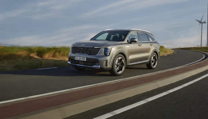 Silver SUV driving on a curved road with wind turbines in the distance.