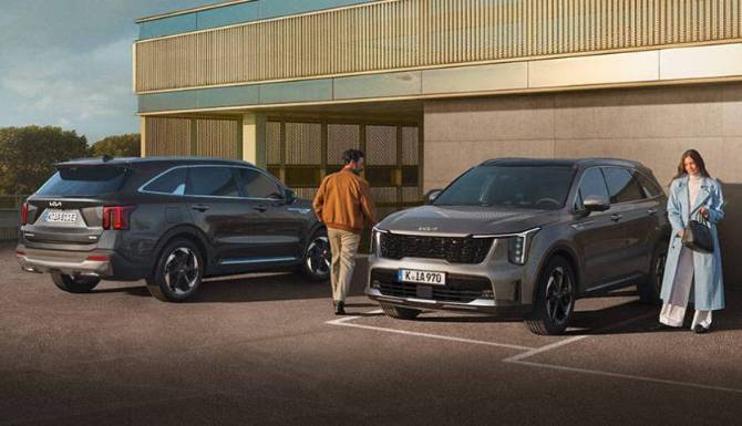 Two people stand beside two grey SUVs parked next to each other.