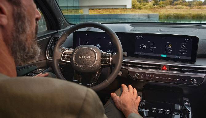 Person in a car interacts with the touchscreen dashboard displaying weather information.