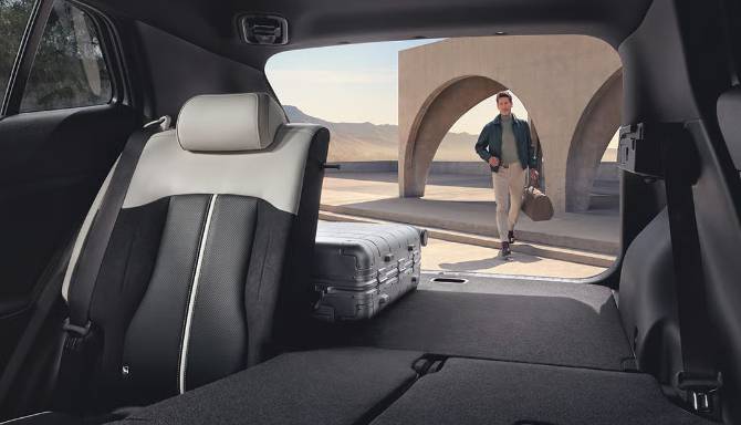 View of car boot with suitcase and a person approaching.