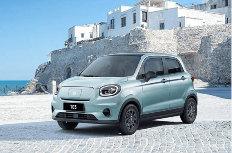 Small light blue car parked on a cobblestone street by stone buildings and the sea.