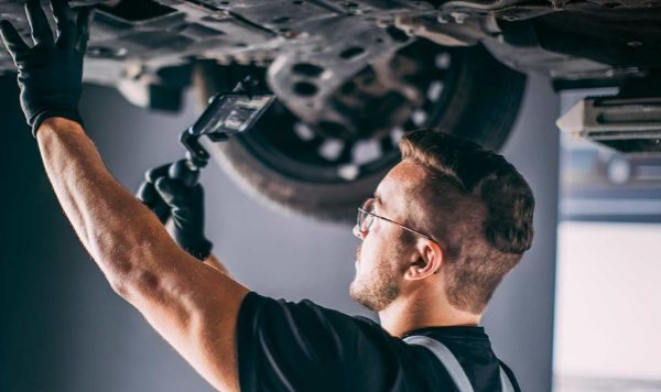 Mechanic inspecting under a car with a torch while wearing gloves and glasses.
