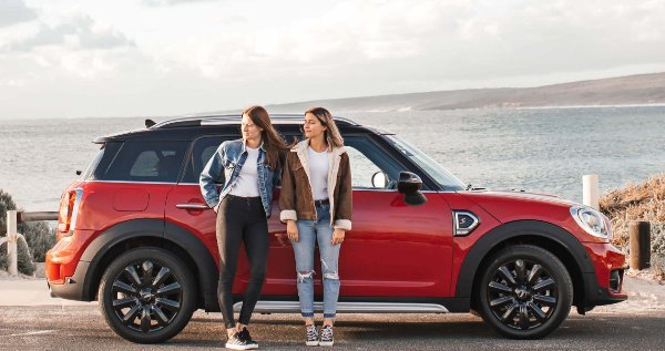 Two people standing next to a red car by the seaside.