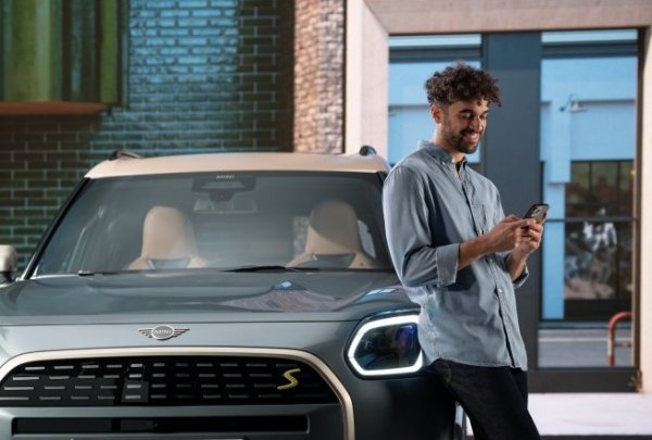 Man leaning on a car while using a smartphone outdoors.