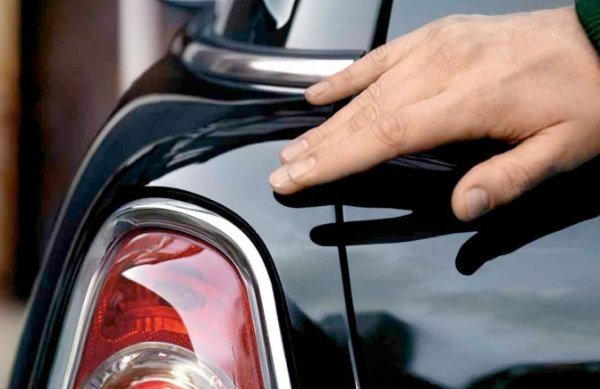 Hand touching the rear of a shiny black car near the taillight.
